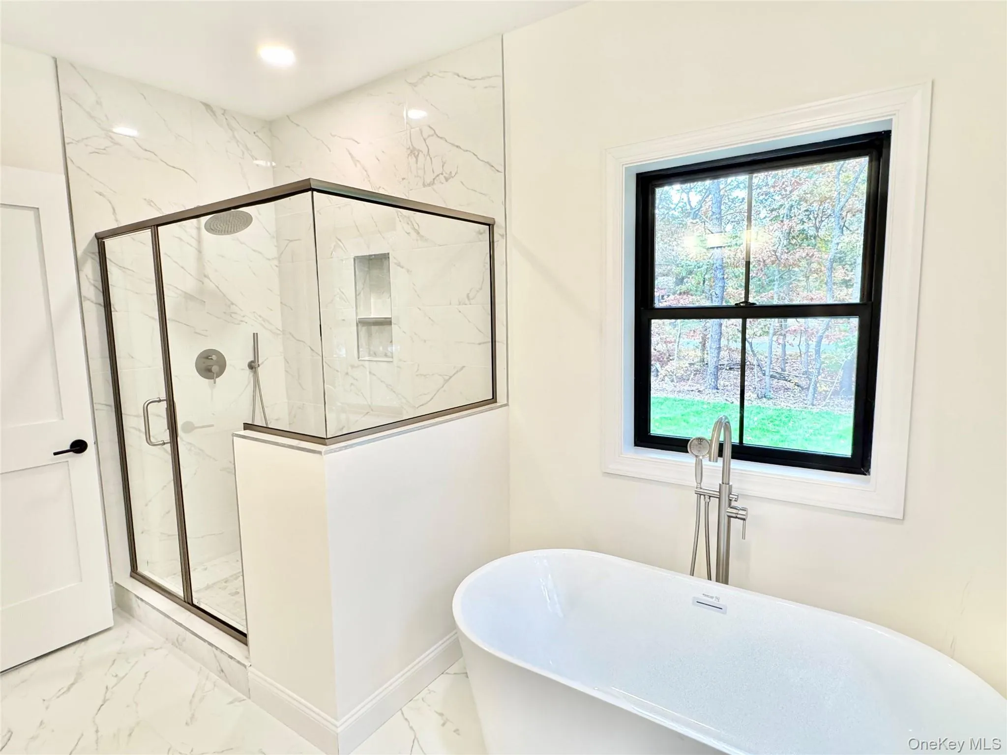 Full bath featuring marble finish floors, a freestanding bath, and a marble finish shower Full bath featuring marble finish floors, a freestanding bath, and a marble finish shower