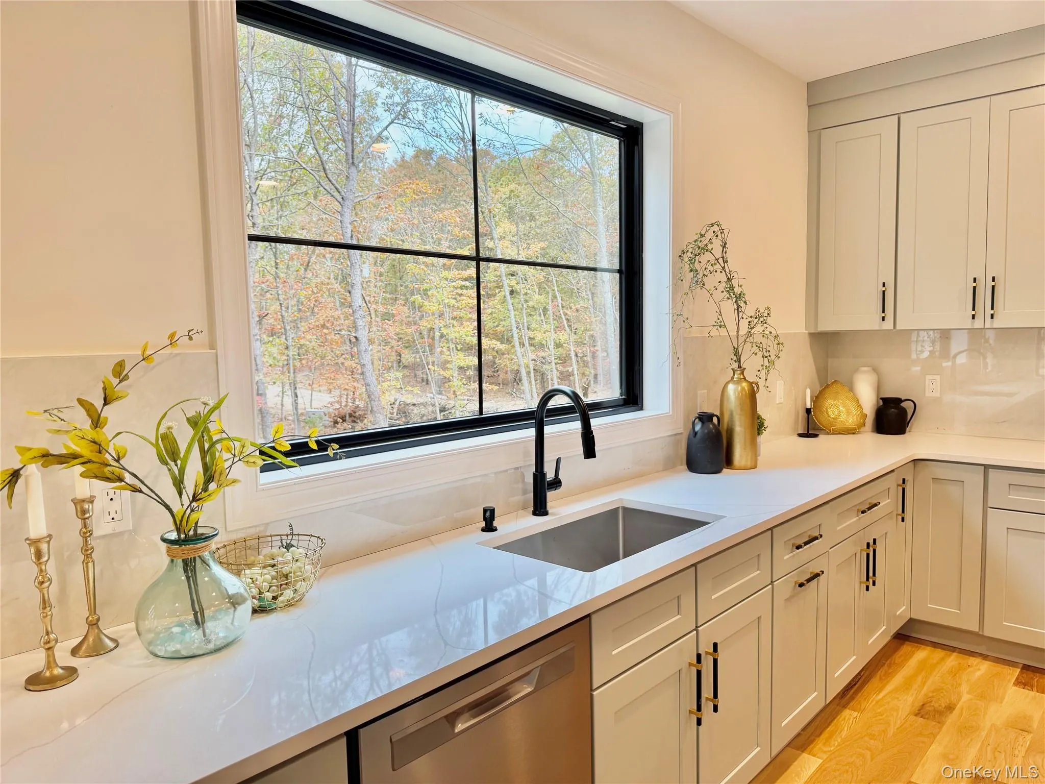 Kitchen with stainless steel dishwasher, light stone counters, tasteful backsplash, and light wood-style flooring Kitchen with stainless steel dishwasher, light stone counters, tasteful backsplash, and light wood-style flooring