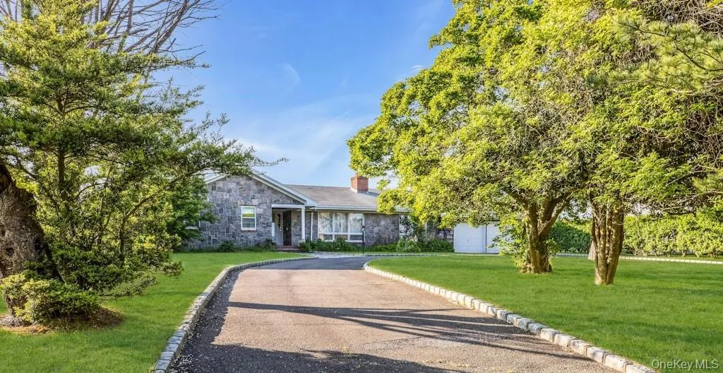 View of front of home with stone siding, a chimney, asphalt driveway, and a front yard View of front of home with stone siding, a chimney, asphalt driveway, and a front yard