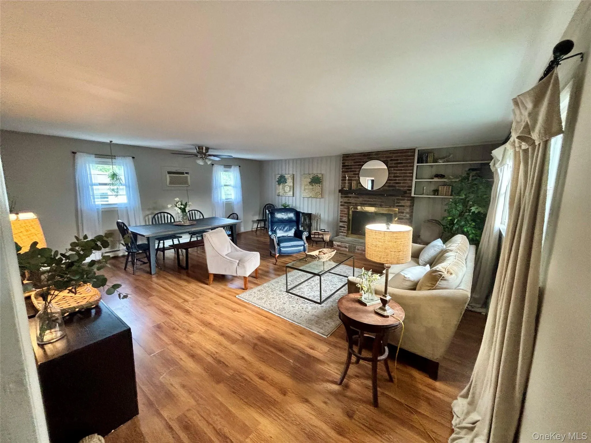 Living room with wood finished floors, a wall unit AC, ceiling fan, built in features, and a brick fireplace Living room with wood finished floors, a wall unit AC, ceiling fan, built in features, and a brick fireplace