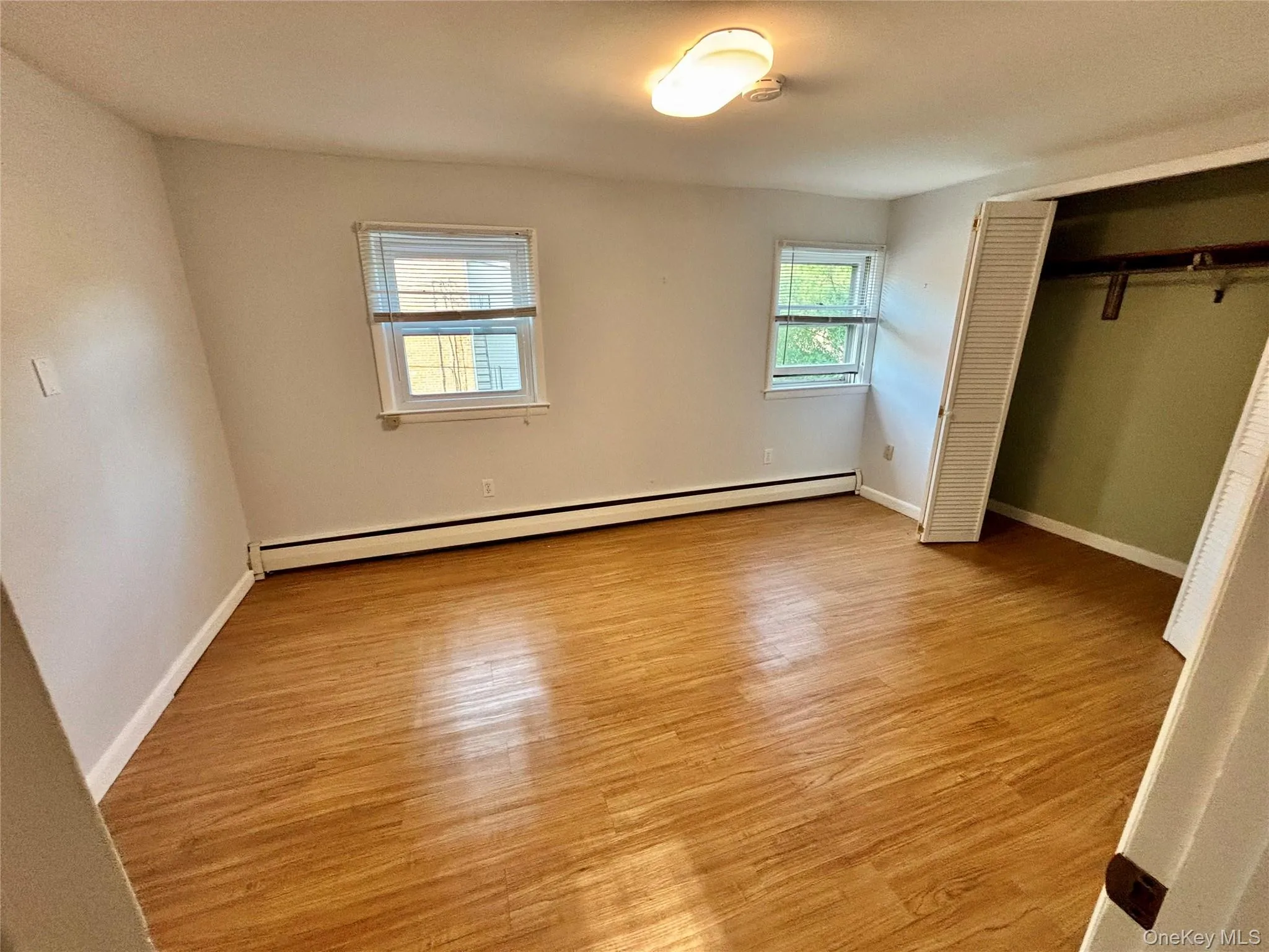 Unfurnished bedroom with baseboard heating, wood finished floors, a closet, and baseboards Unfurnished bedroom with baseboard heating, wood finished floors, a closet, and baseboards