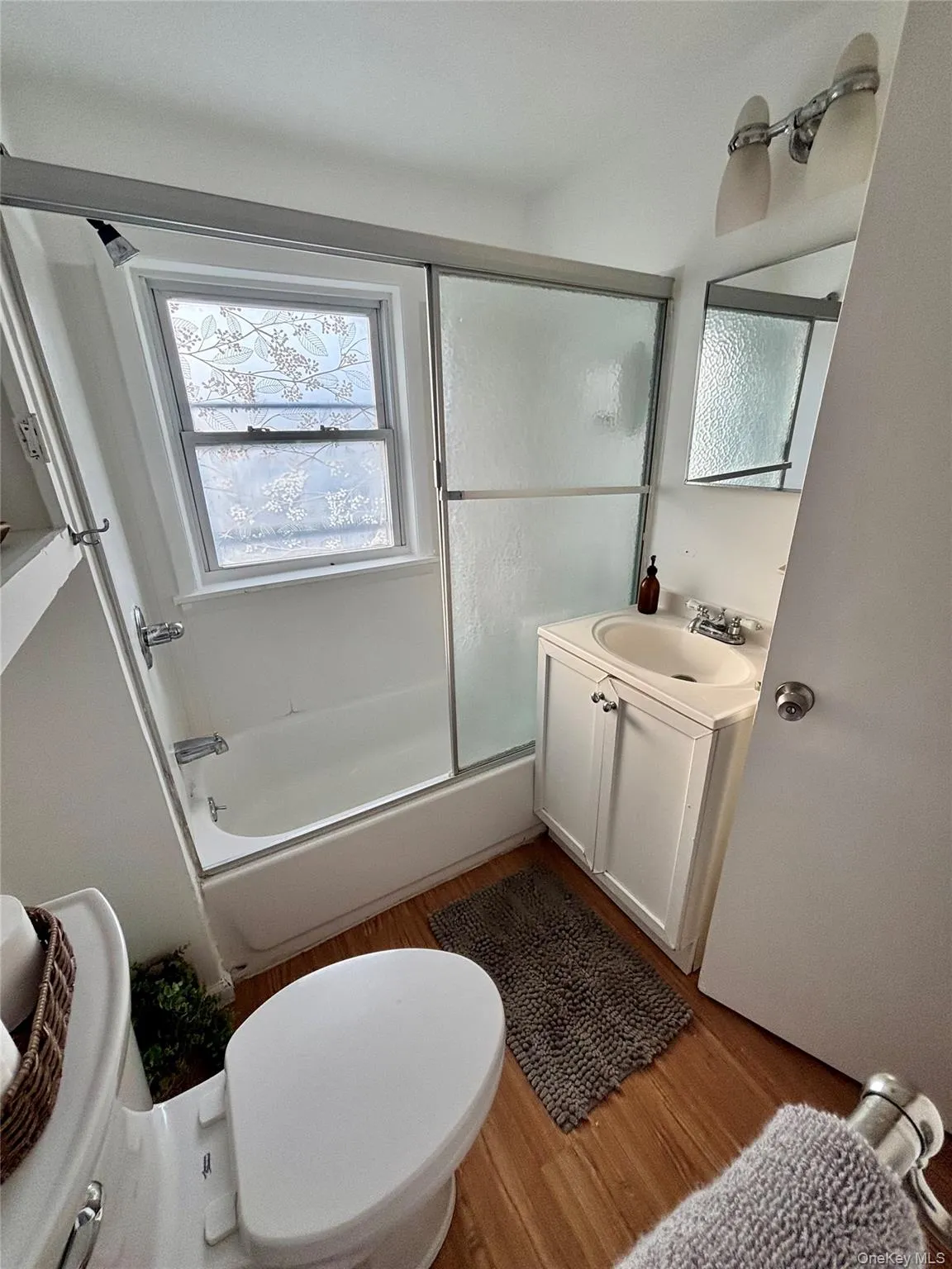Bathroom with wood finished floors, vanity, toilet, and shower / bath combination with glass door Bathroom with wood finished floors, vanity, toilet, and shower / bath combination with glass door