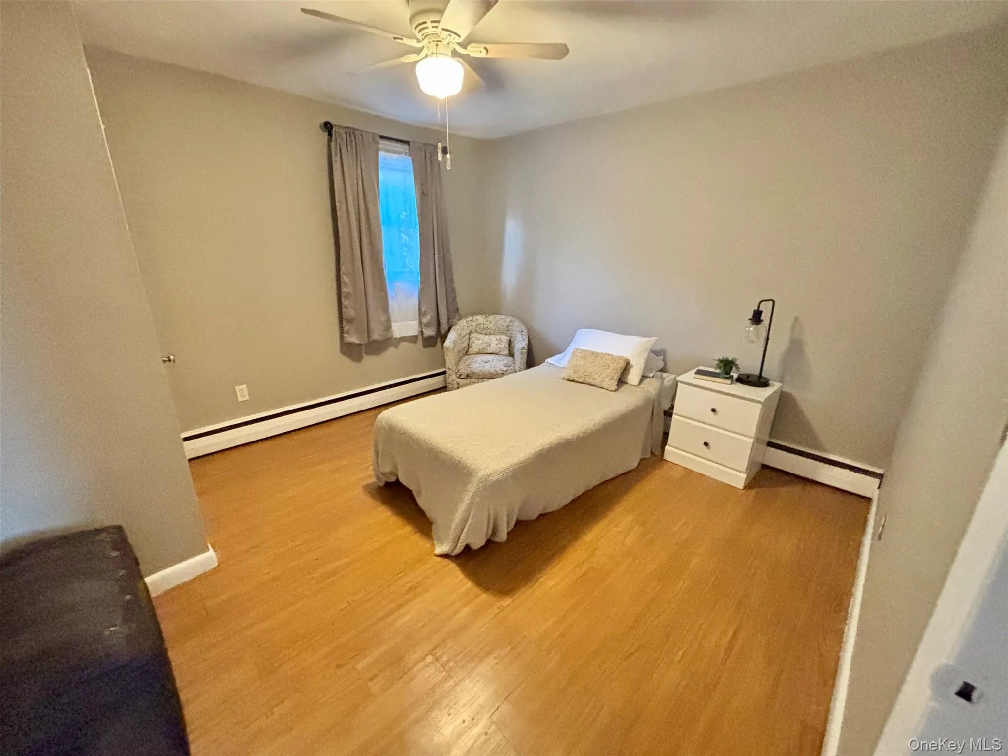 Bedroom with baseboard heating, light wood-type flooring, and baseboards Bedroom with baseboard heating, light wood-type flooring, and baseboards