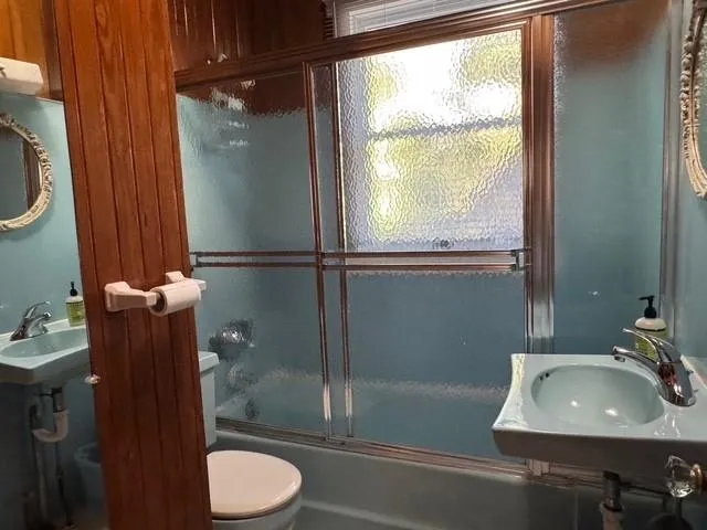 Full bathroom featuring toilet, bath / shower combo with glass door, and a sink Full bathroom featuring toilet, bath / shower combo with glass door, and a sink
