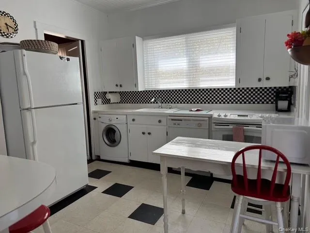 Kitchen with washer / clothes dryer, white appliances, a sink, light flooring, and backsplash Kitchen with washer / clothes dryer, white appliances, a sink, light flooring, and backsplash