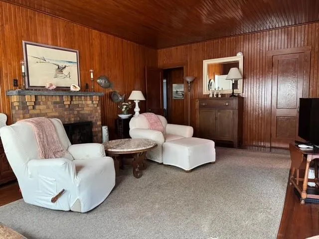 Living area with wood walls, a brick fireplace, wood ceiling, and carpet flooring Living area with wood walls, a brick fireplace, wood ceiling, and carpet flooring