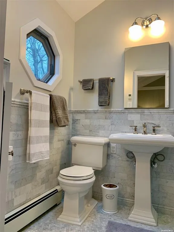 Bathroom with baseboard heating, toilet, tile walls, a wainscoted wall, and lofted ceiling Bathroom with baseboard heating, toilet, tile walls, a wainscoted wall, and lofted ceiling