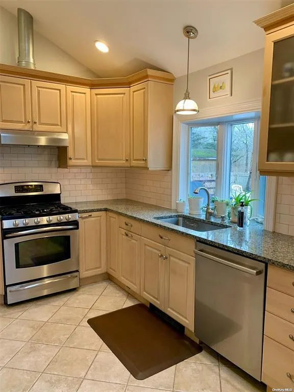 Kitchen featuring appliances with stainless steel finishes, under cabinet range hood, a sink, lofted ceiling, and tasteful backsplash Kitchen featuring appliances with stainless steel finishes, under cabinet range hood, a sink, lofted ceiling, and tasteful backsplash