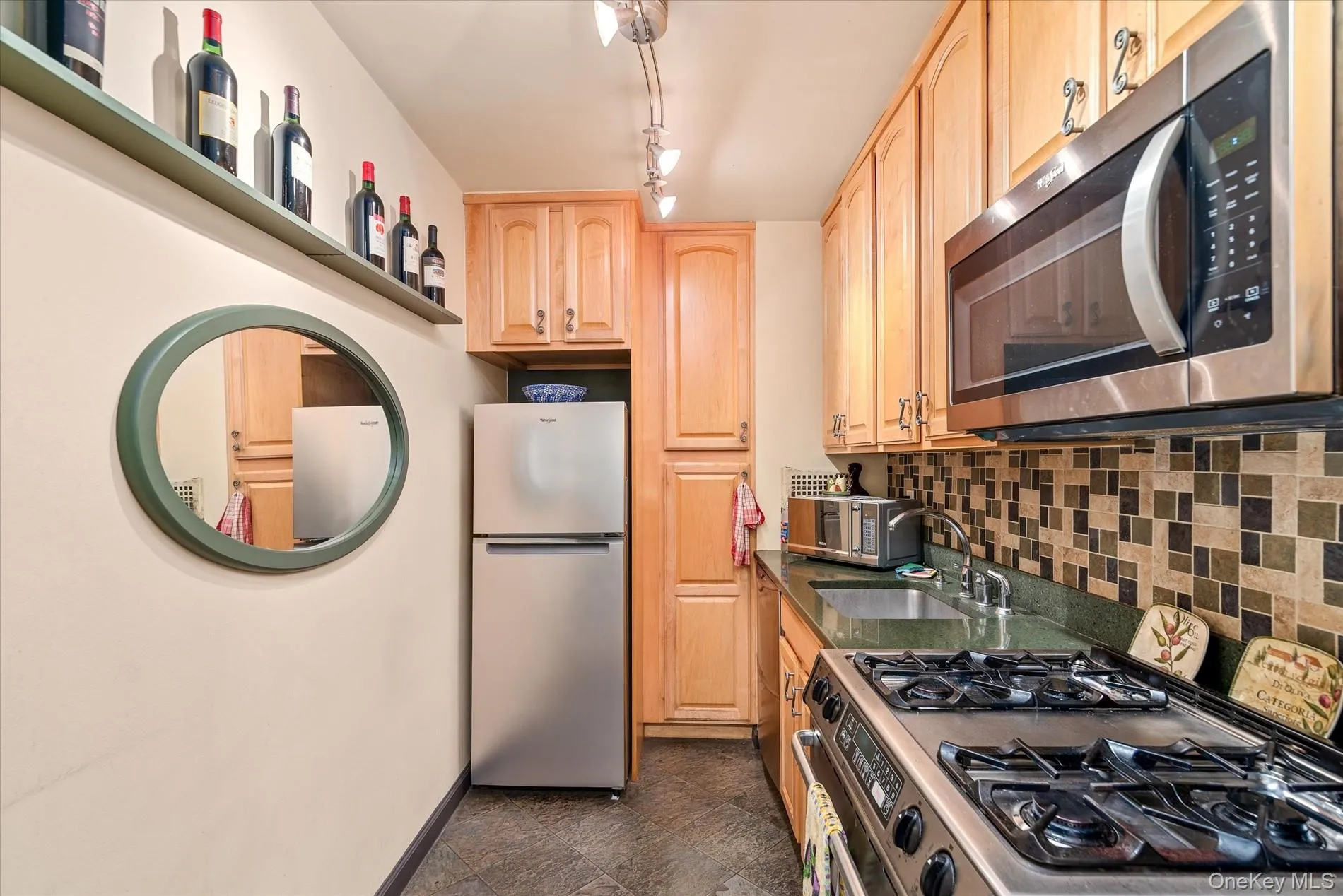 Kitchen featuring appliances with stainless steel finishes, light brown cabinetry, backsplash, a sink, and dark countertops Kitchen featuring appliances with stainless steel finishes, light brown cabinetry, backsplash, a sink, and dark countertops