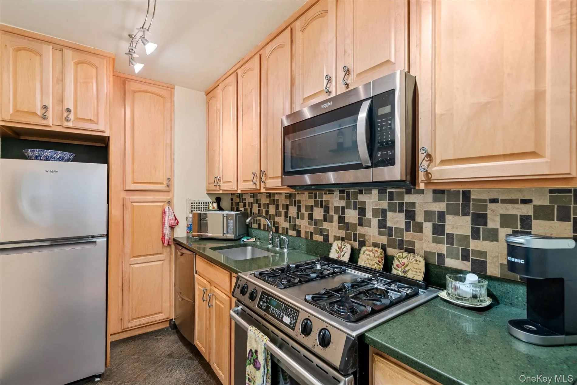Kitchen with stainless steel appliances, light brown cabinets, a sink, decorative backsplash, and dark countertops Kitchen with stainless steel appliances, light brown cabinets, a sink, decorative backsplash, and dark countertops