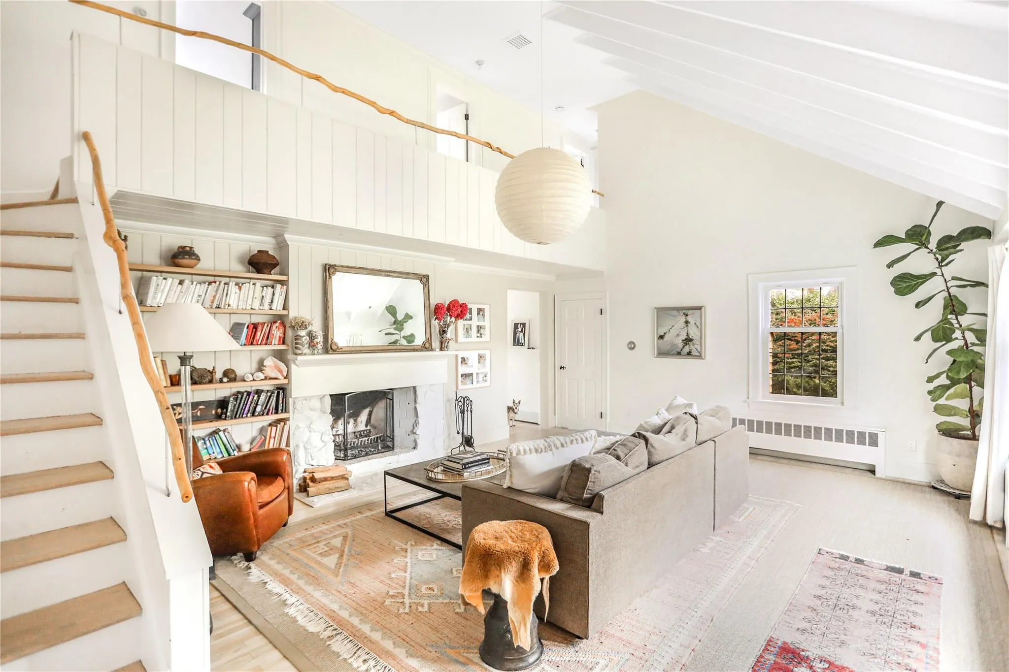 Living area featuring radiator heating unit, wood finished floors, stairs, a fireplace with raised hearth, and high vaulted ceiling Living area featuring radiator heating unit, wood finished floors, stairs, a fireplace with raised hearth, and high vaulted ceiling