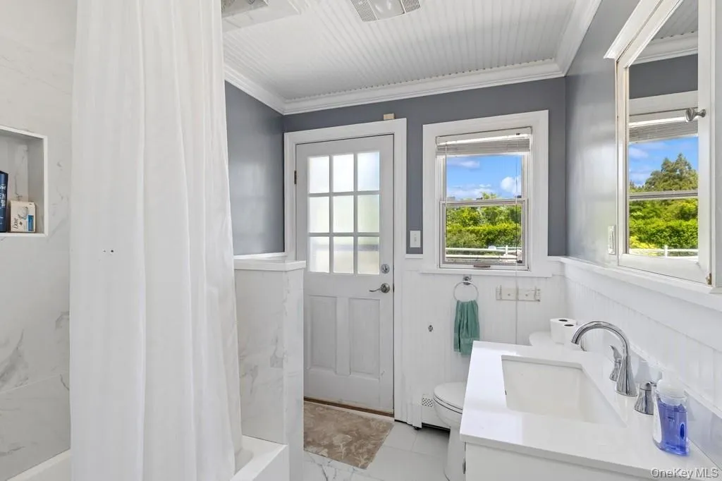 Full bathroom featuring wainscoting, ornamental molding, toilet, vanity, and shower / bath combo Full bathroom featuring wainscoting, ornamental molding, toilet, vanity, and shower / bath combo