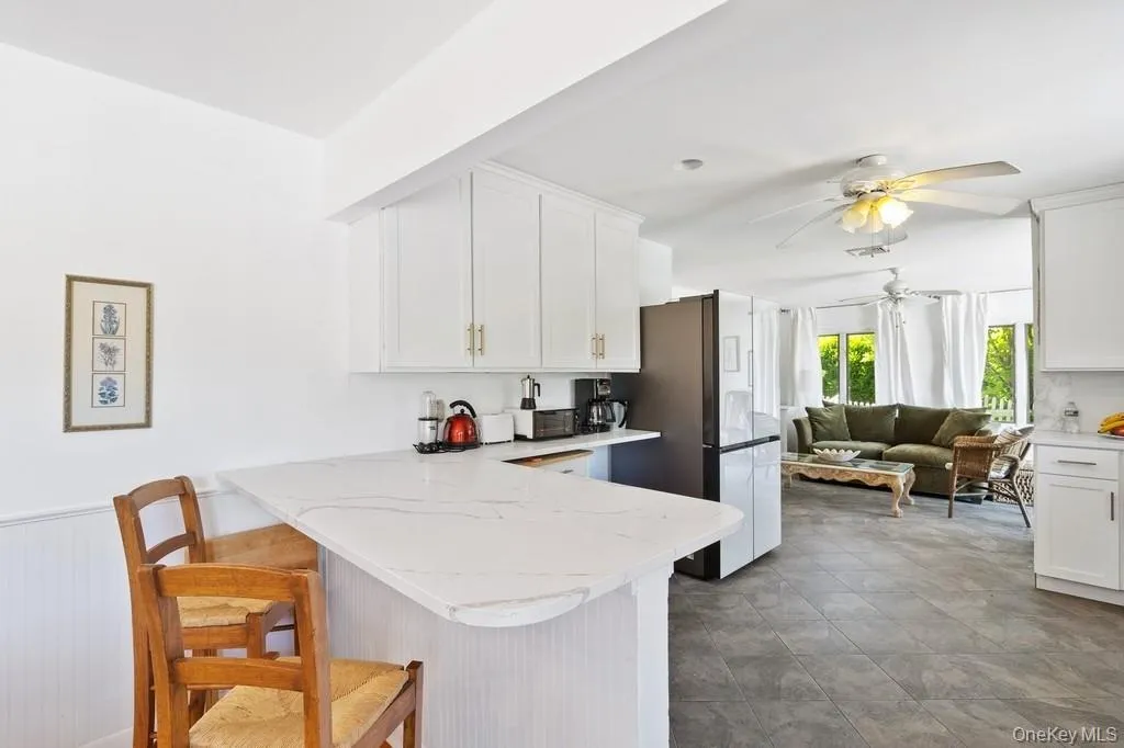 Kitchen featuring white cabinetry, a peninsula, a breakfast bar, and a wainscoted wall Kitchen featuring white cabinetry, a peninsula, a breakfast bar, and a wainscoted wall