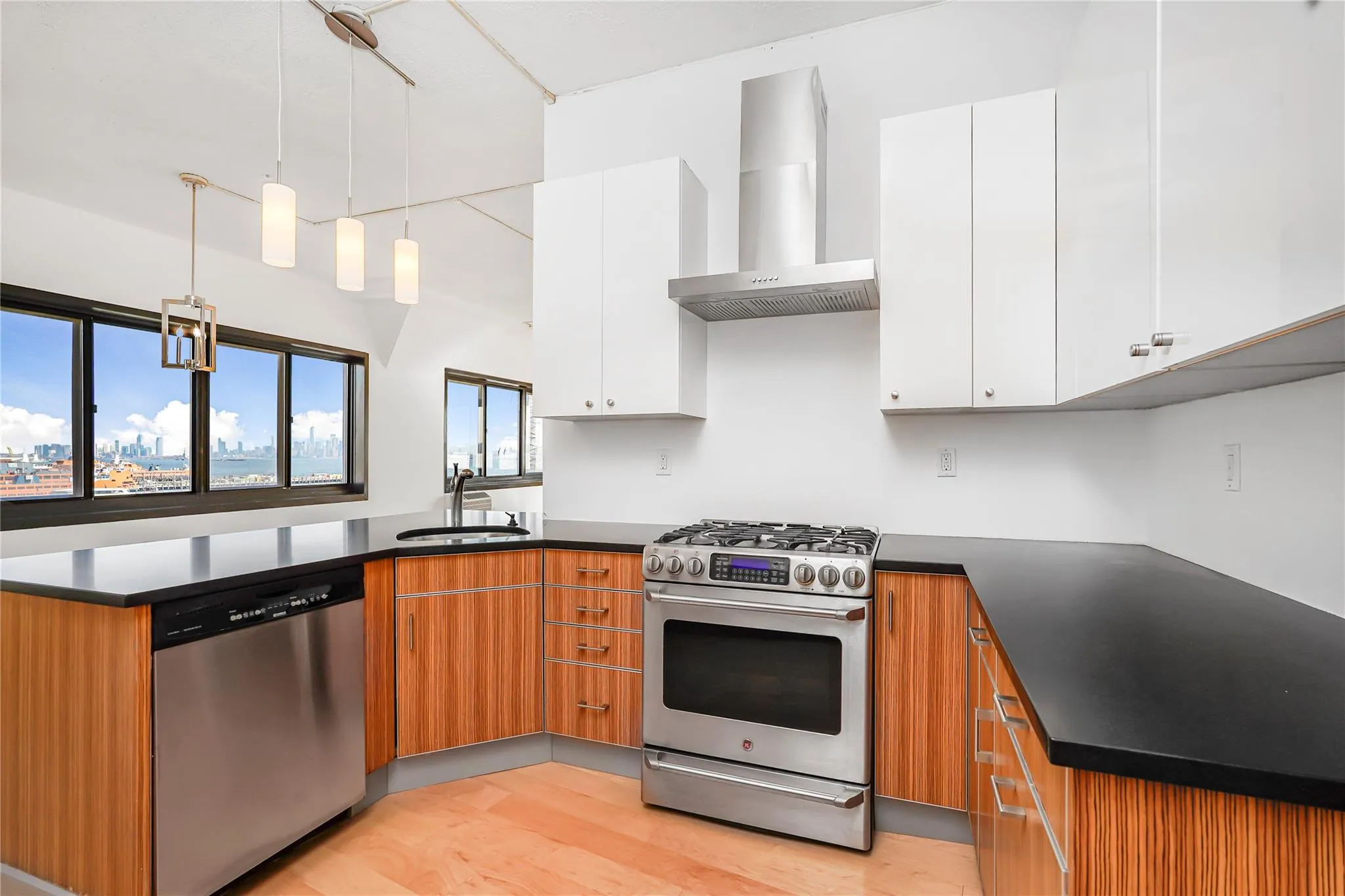 Kitchen with stainless steel appliances, wall chimney exhaust hood, a sink, a peninsula, and light wood-type flooring Kitchen with stainless steel appliances, wall chimney exhaust hood, a sink, a peninsula, and light wood-type flooring
