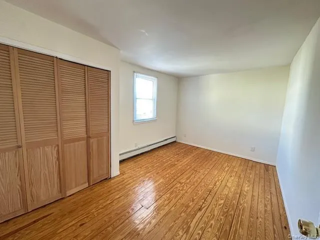 Unfurnished bedroom with light wood finished floors, a baseboard radiator, and a closet Unfurnished bedroom with light wood finished floors, a baseboard radiator, and a closet