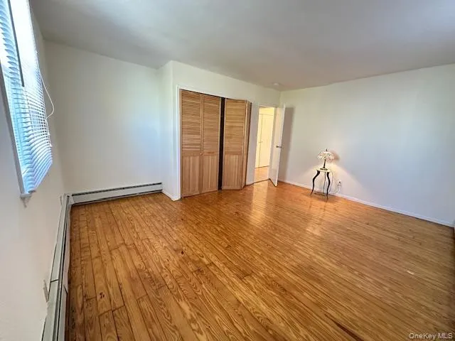 Unfurnished bedroom featuring light wood-style floors, a closet, and a baseboard radiator Unfurnished bedroom featuring light wood-style floors, a closet, and a baseboard radiator
