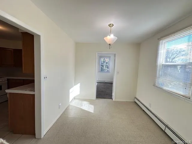 Unfurnished dining area featuring a baseboard radiator, healthy amount of natural light, and light carpet Unfurnished dining area featuring a baseboard radiator, healthy amount of natural light, and light carpet