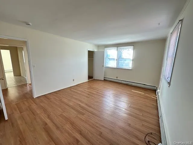 Empty room featuring light wood-type flooring and a baseboard heating unit Empty room featuring light wood-type flooring and a baseboard heating unit