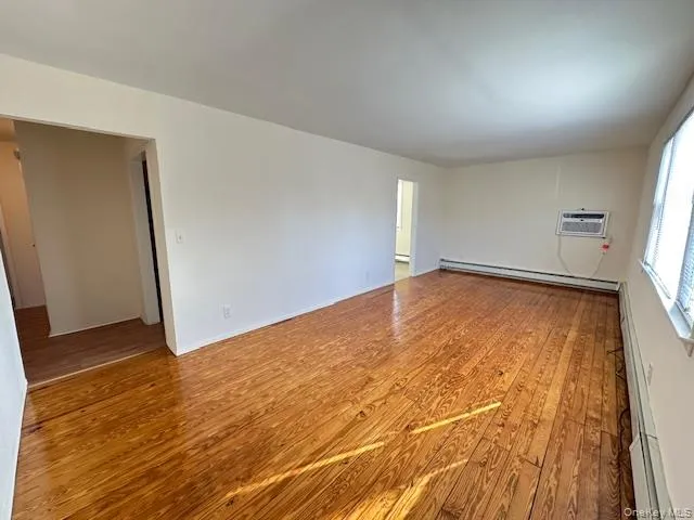 Spare room featuring light wood-style floors, a baseboard radiator, and a wall mounted air conditioner Spare room featuring light wood-style floors, a baseboard radiator, and a wall mounted air conditioner