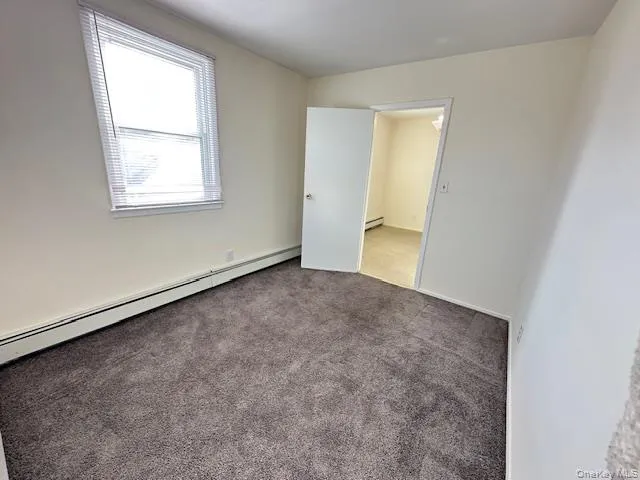 Carpeted empty room with baseboard heating and a baseboard radiator Carpeted empty room with baseboard heating and a baseboard radiator