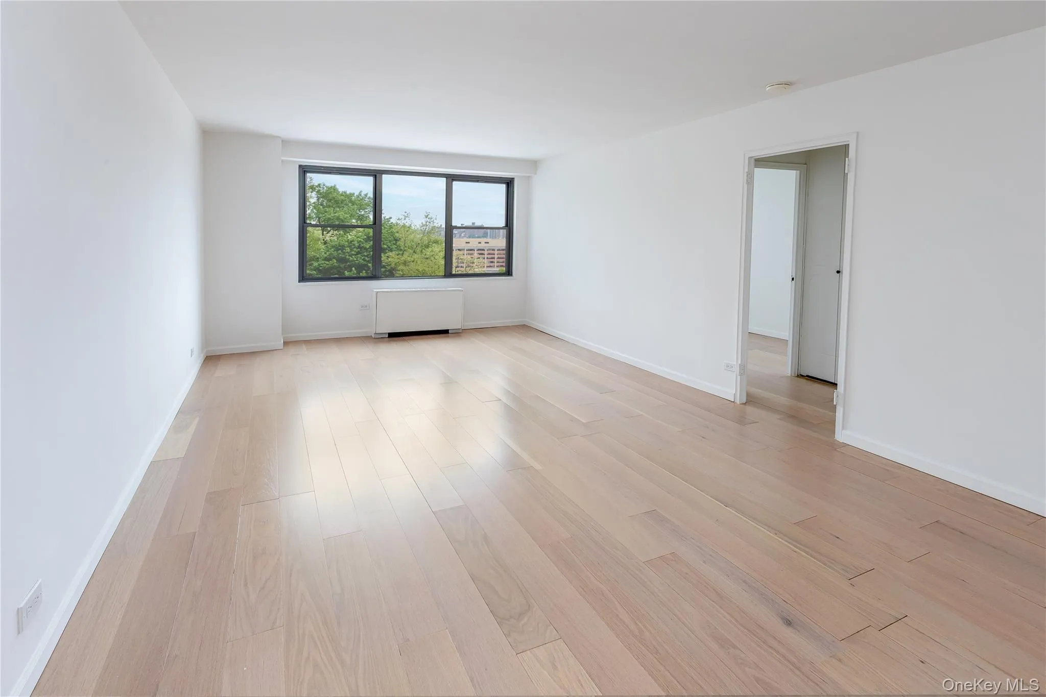 Empty room featuring light wood finished floors, radiator heating unit, a smoke detector, and baseboards Empty room featuring light wood finished floors, radiator heating unit, a smoke detector, and baseboards