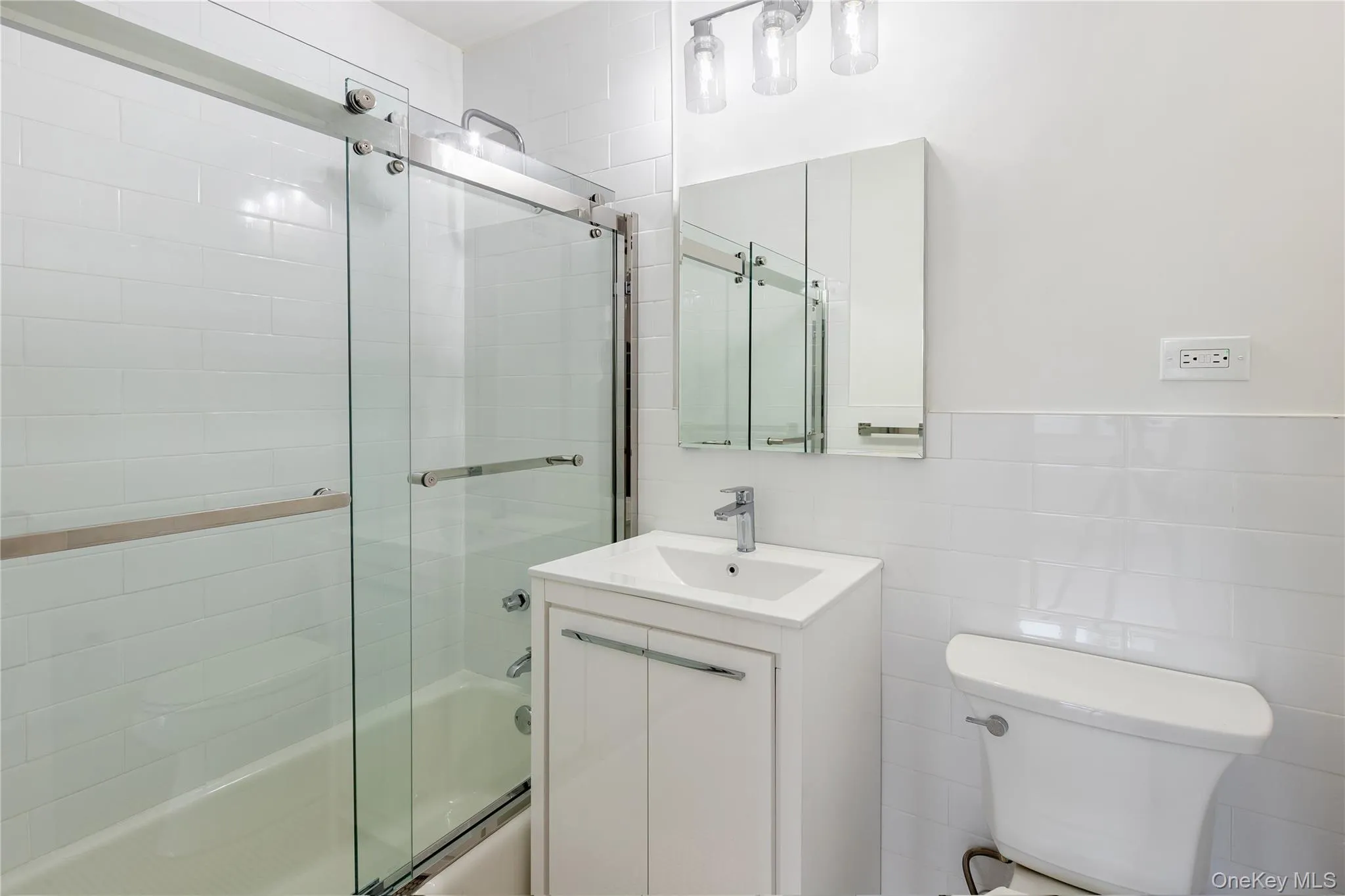 Full bathroom with toilet, combined bath / shower with glass door, vanity, and tile walls Full bathroom with toilet, combined bath / shower with glass door, vanity, and tile walls