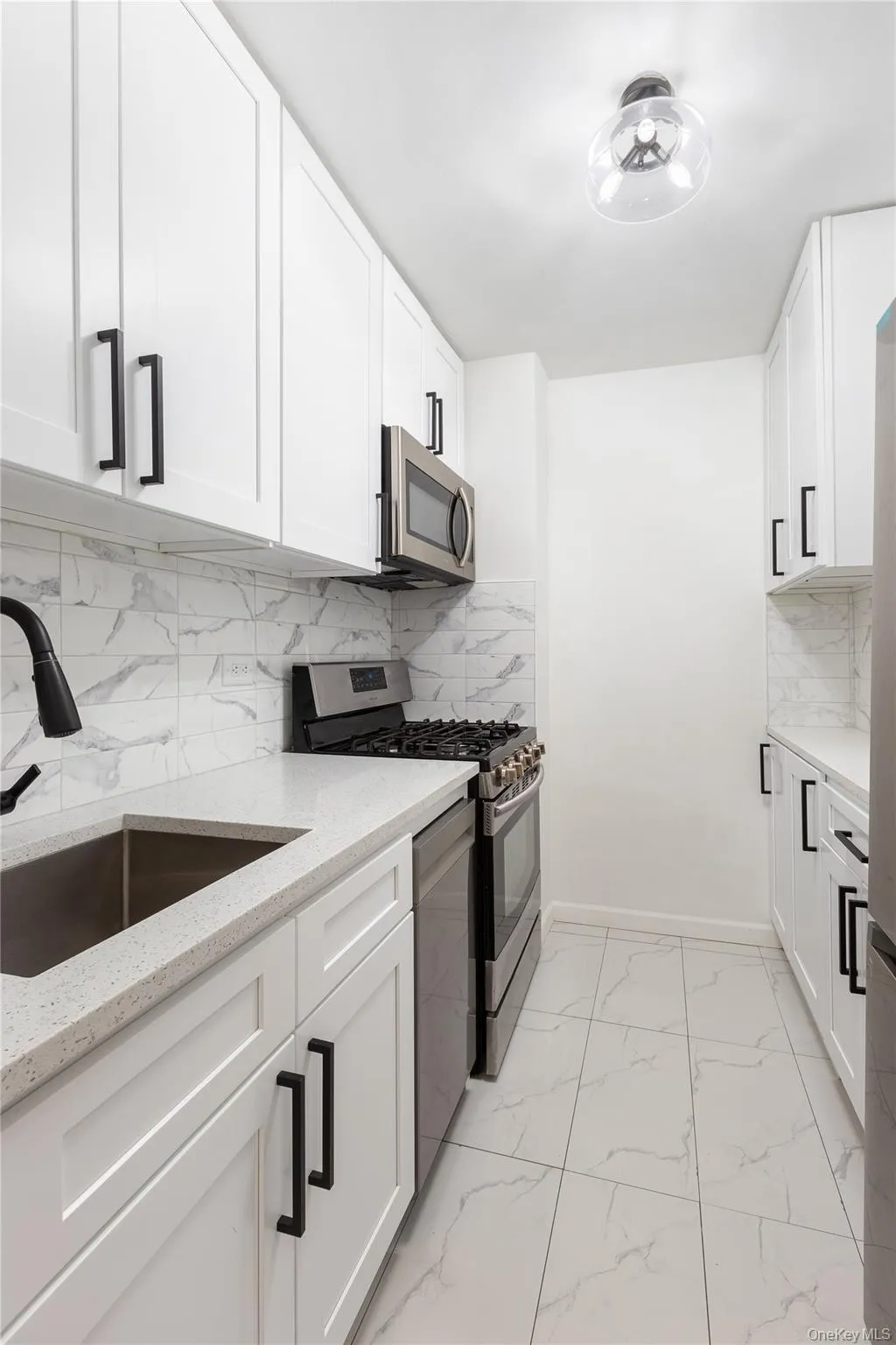 Kitchen featuring appliances with stainless steel finishes, a sink, light stone counters, baseboards, and white cabinets Kitchen featuring appliances with stainless steel finishes, a sink, light stone counters, baseboards, and white cabinets