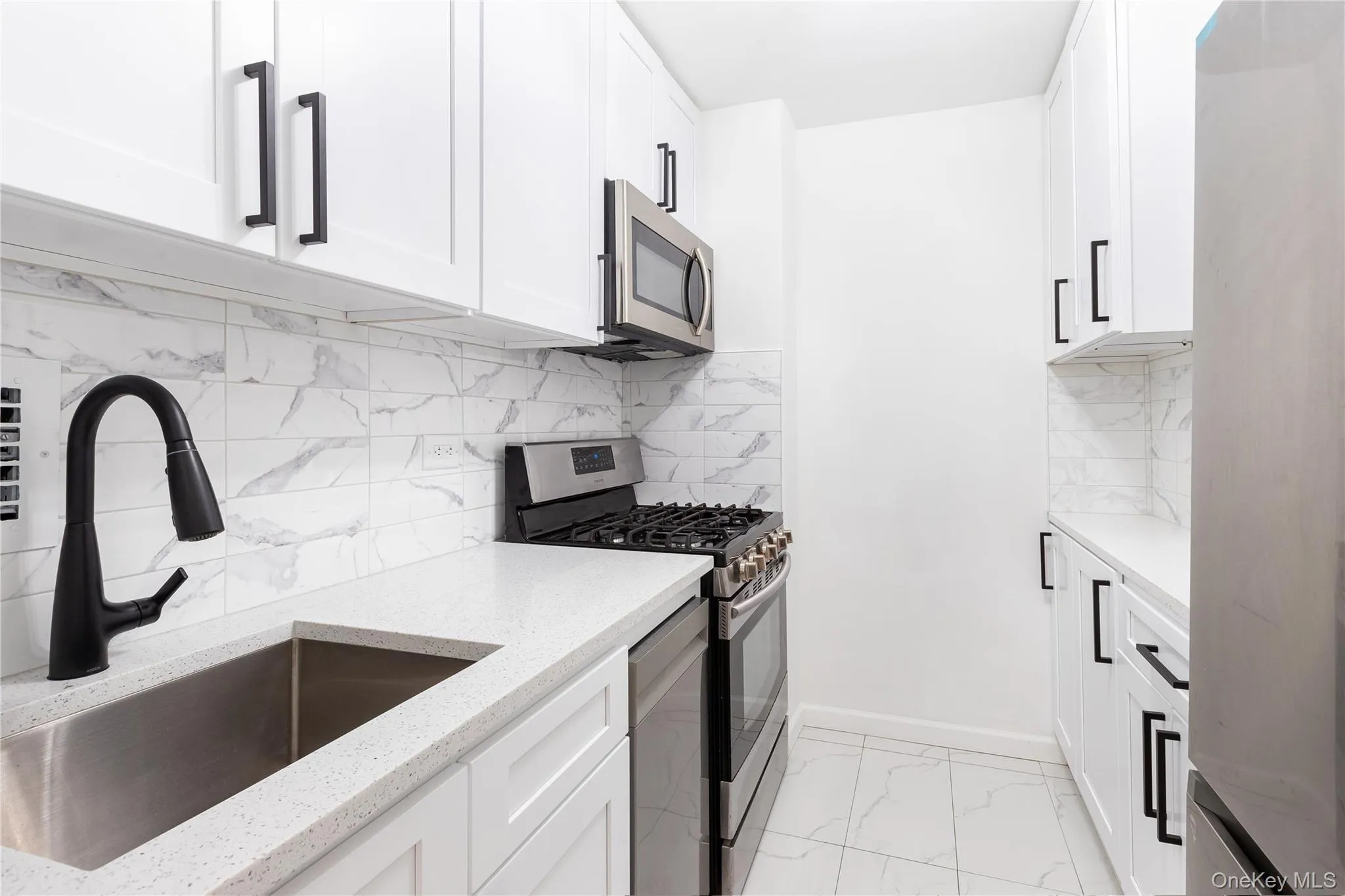Kitchen with stainless steel appliances, a sink, light marble finish flooring, light stone counters, and white cabinetry Kitchen with stainless steel appliances, a sink, light marble finish flooring, light stone counters, and white cabinetry