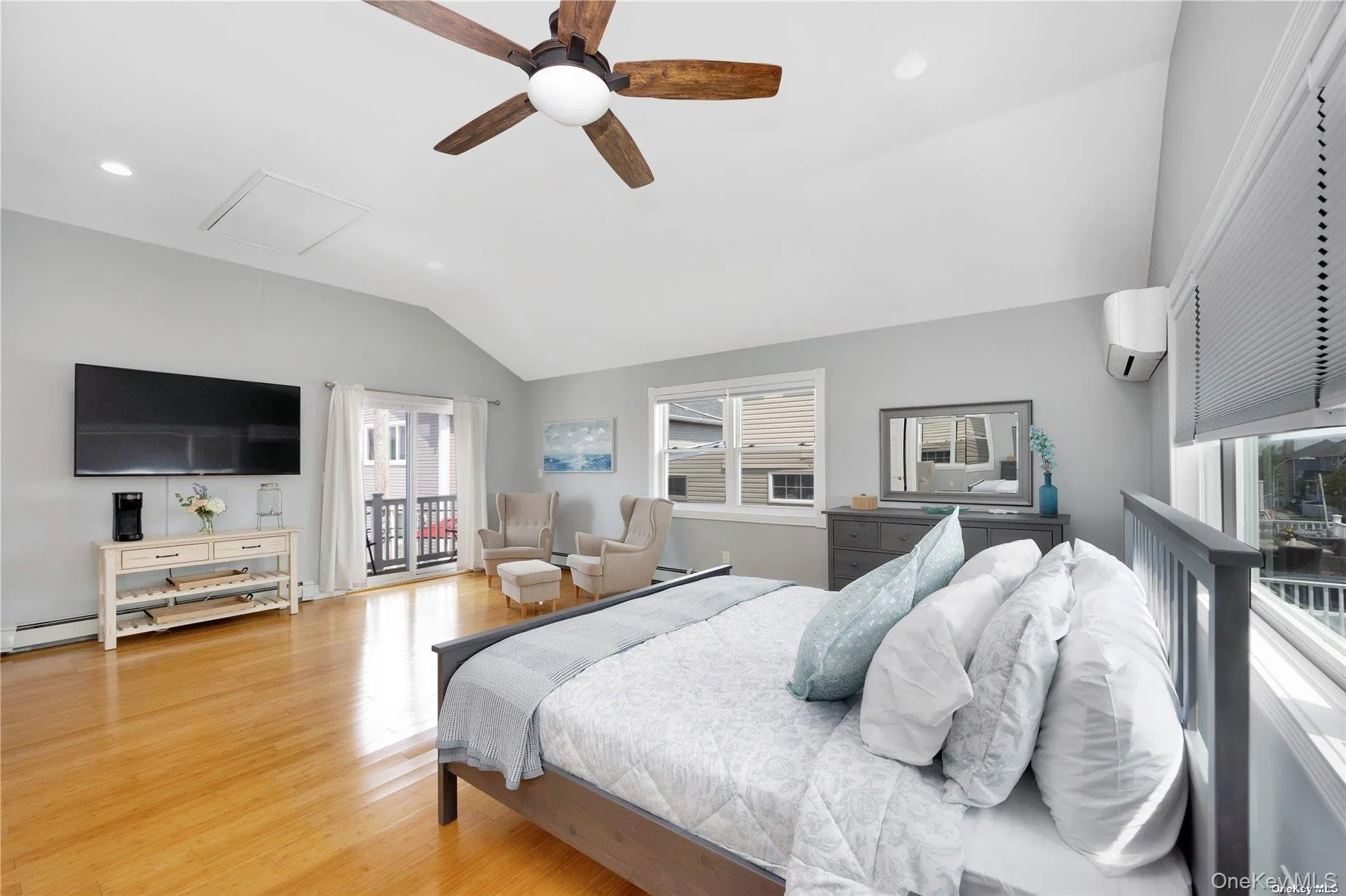 Bedroom featuring attic access, vaulted ceiling, wood finished floors, access to outside, and baseboard heating Bedroom featuring attic access, vaulted ceiling, wood finished floors, access to outside, and baseboard heating