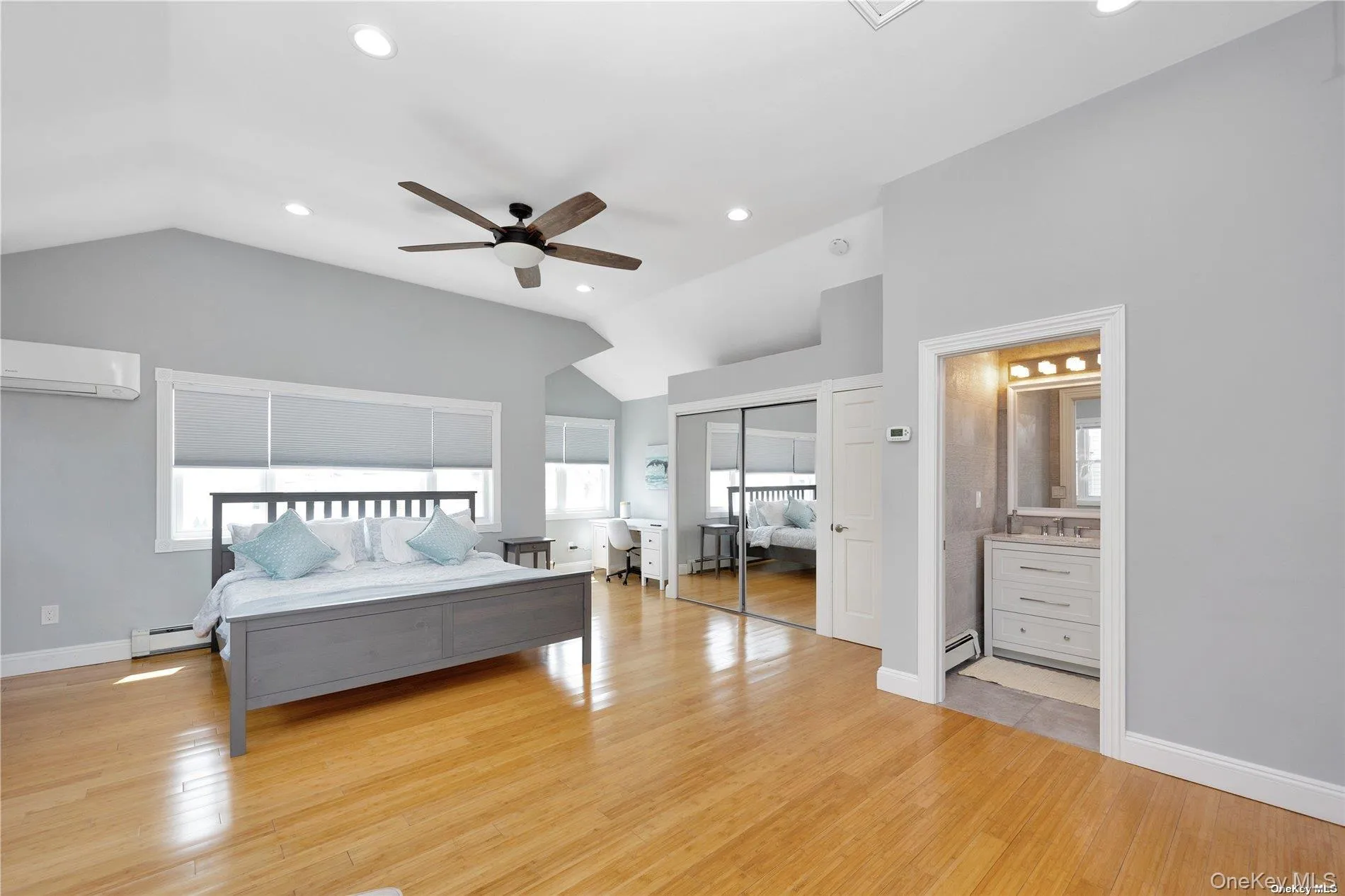 Bedroom featuring vaulted ceiling, a wall mounted air conditioner, a baseboard radiator, light wood-style flooring, and recessed lighting Bedroom featuring vaulted ceiling, a wall mounted air conditioner, a baseboard radiator, light wood-style flooring, and recessed lighting