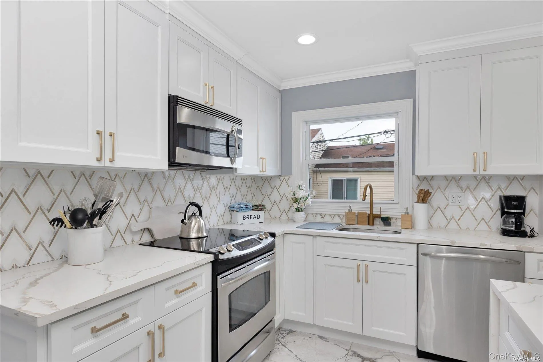 Kitchen featuring stainless steel appliances, a sink, white cabinets, ornamental molding, and light stone countertops Kitchen featuring stainless steel appliances, a sink, white cabinets, ornamental molding, and light stone countertops