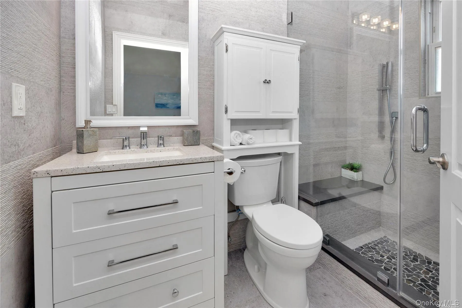 Full bathroom with a shower stall, toilet, vanity, and wallpapered walls Full bathroom with a shower stall, toilet, vanity, and wallpapered walls