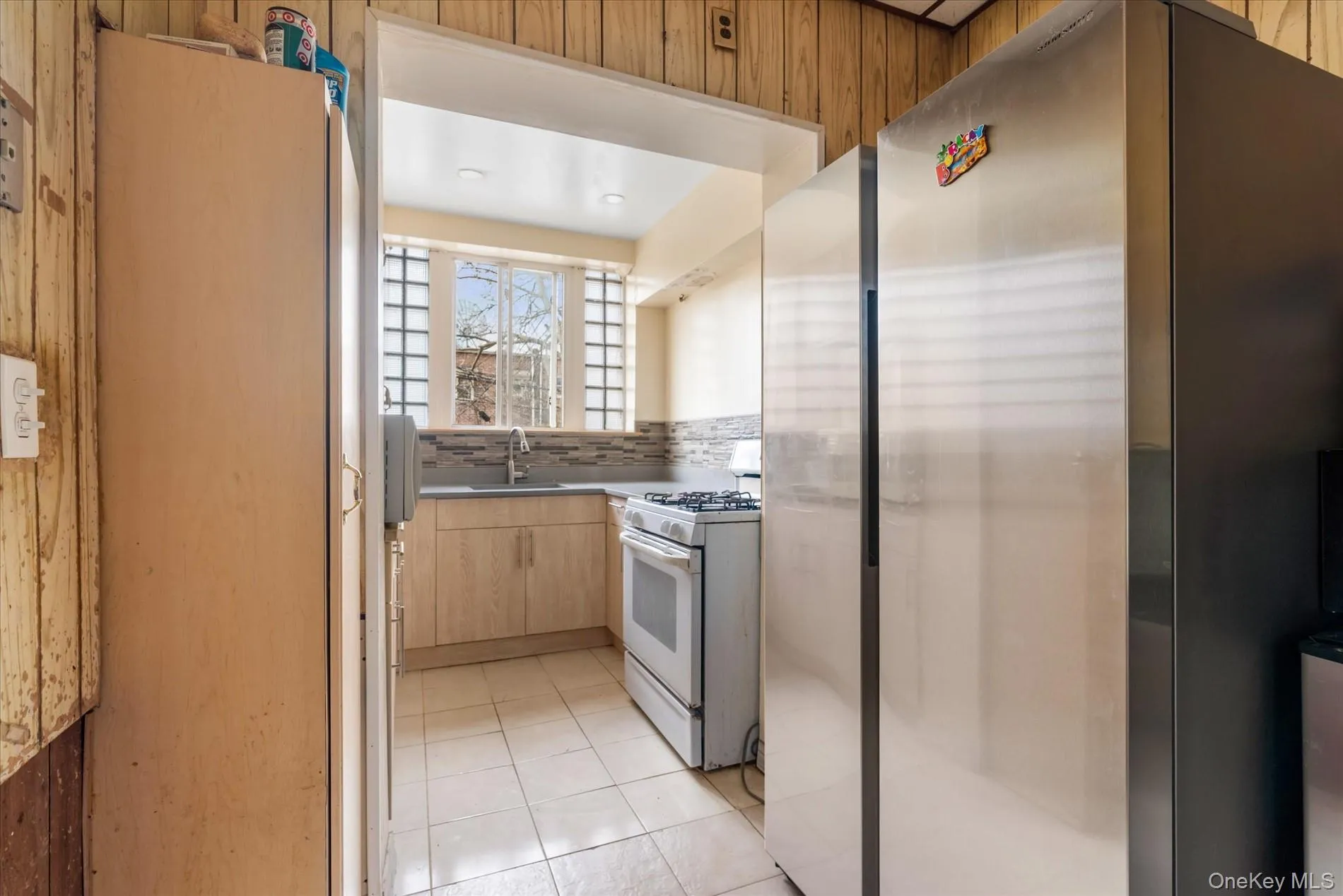 Kitchen featuring white gas stove, a sink, freestanding refrigerator, light brown cabinetry, and light tile patterned floors Kitchen featuring white gas stove, a sink, freestanding refrigerator, light brown cabinetry, and light tile patterned floors