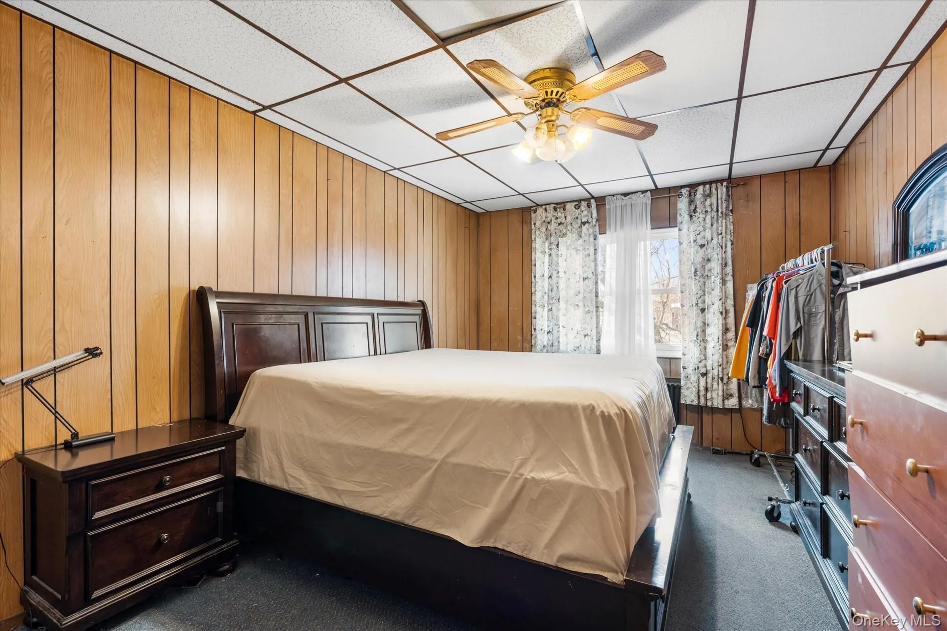Carpeted bedroom featuring a drop ceiling, wood walls, and a ceiling fan Carpeted bedroom featuring a drop ceiling, wood walls, and a ceiling fan