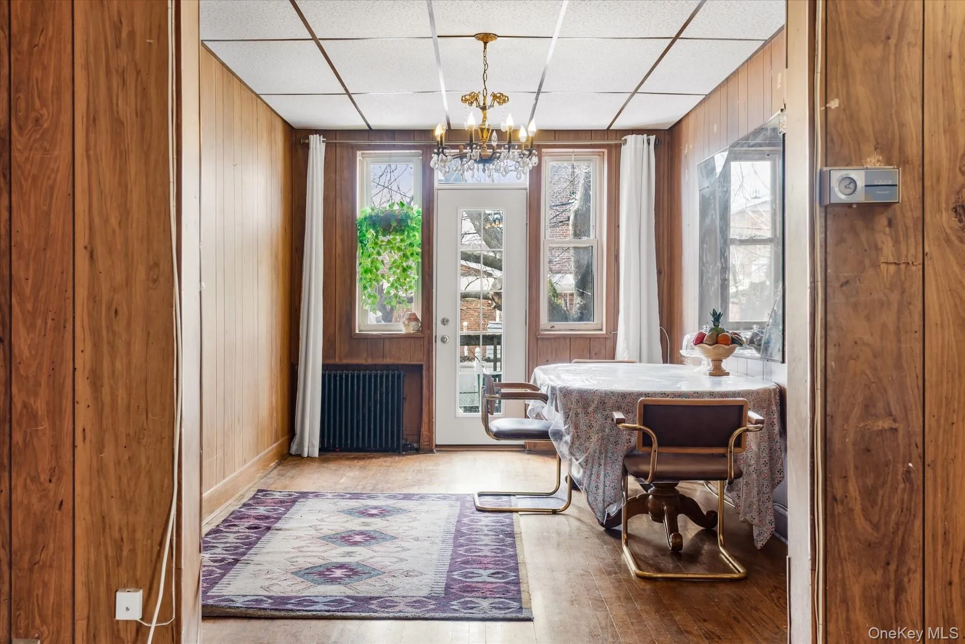 Dining room with radiator heating unit, wooden walls, a chandelier, a paneled ceiling, and wood finished floors Dining room with radiator heating unit, wooden walls, a chandelier, a paneled ceiling, and wood finished floors