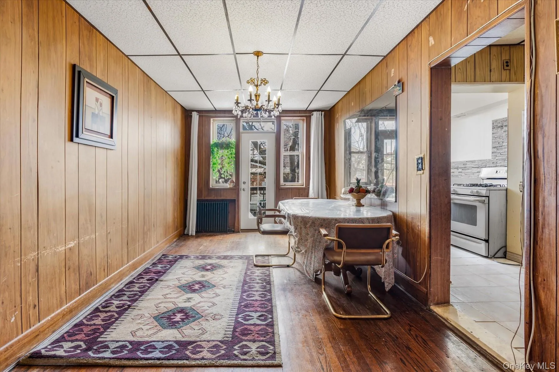 Dining room with a chandelier, wood walls, light wood finished floors, and a drop ceiling Dining room with a chandelier, wood walls, light wood finished floors, and a drop ceiling