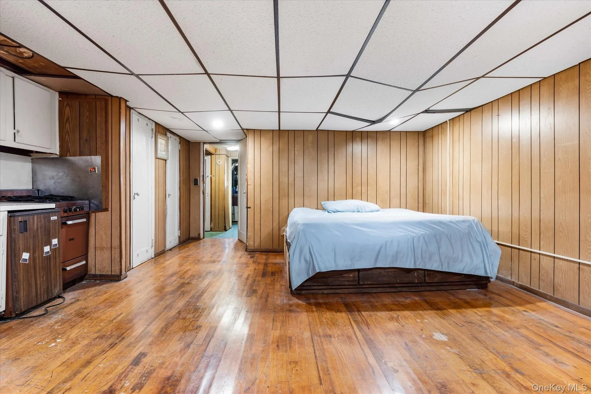 Bedroom featuring light wood-type flooring, a paneled ceiling, and wooden walls Bedroom featuring light wood-type flooring, a paneled ceiling, and wooden walls