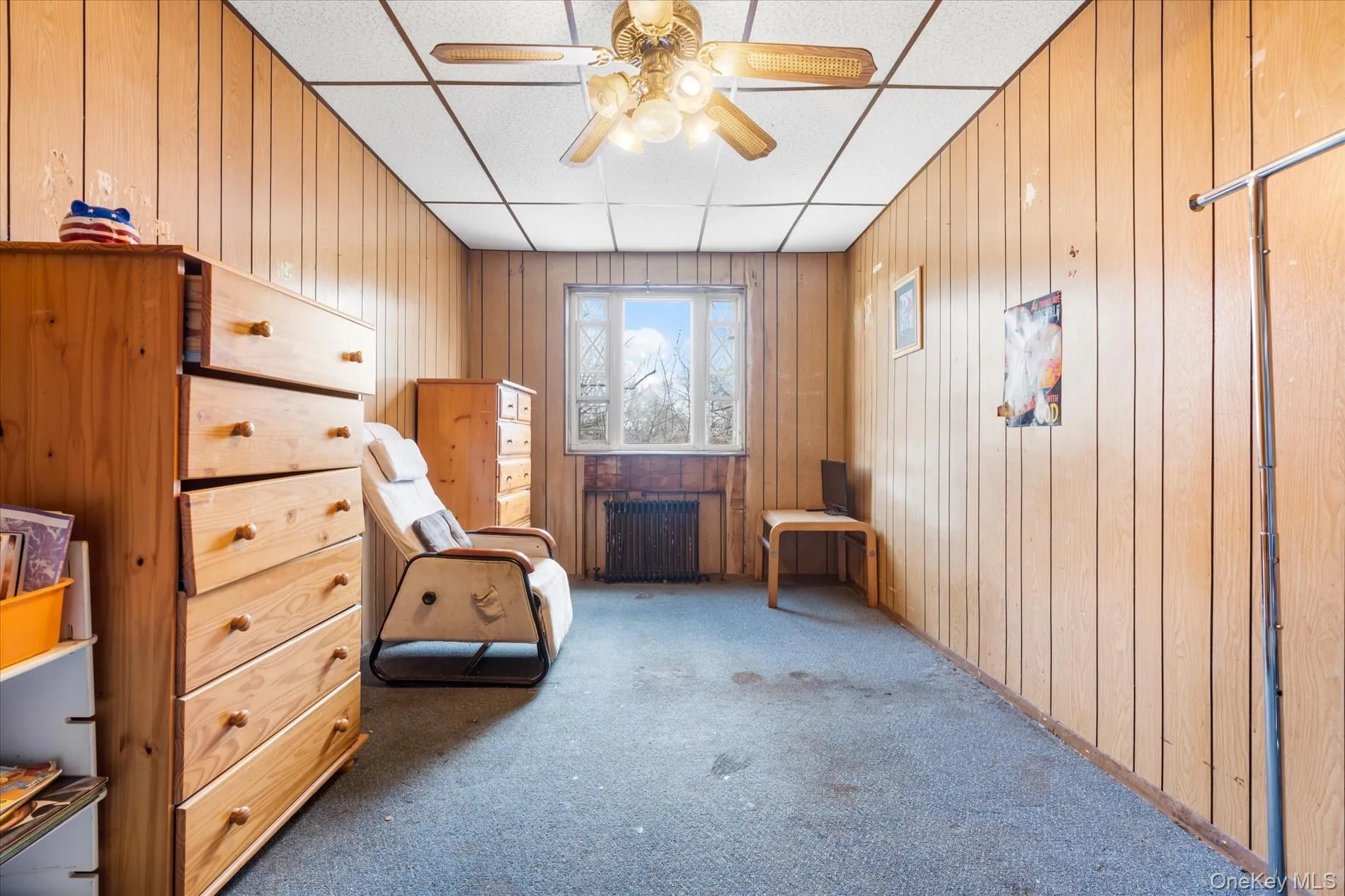 Sitting room featuring radiator, carpet, a drop ceiling, wood walls, and a ceiling fan Sitting room featuring radiator, carpet, a drop ceiling, wood walls, and a ceiling fan