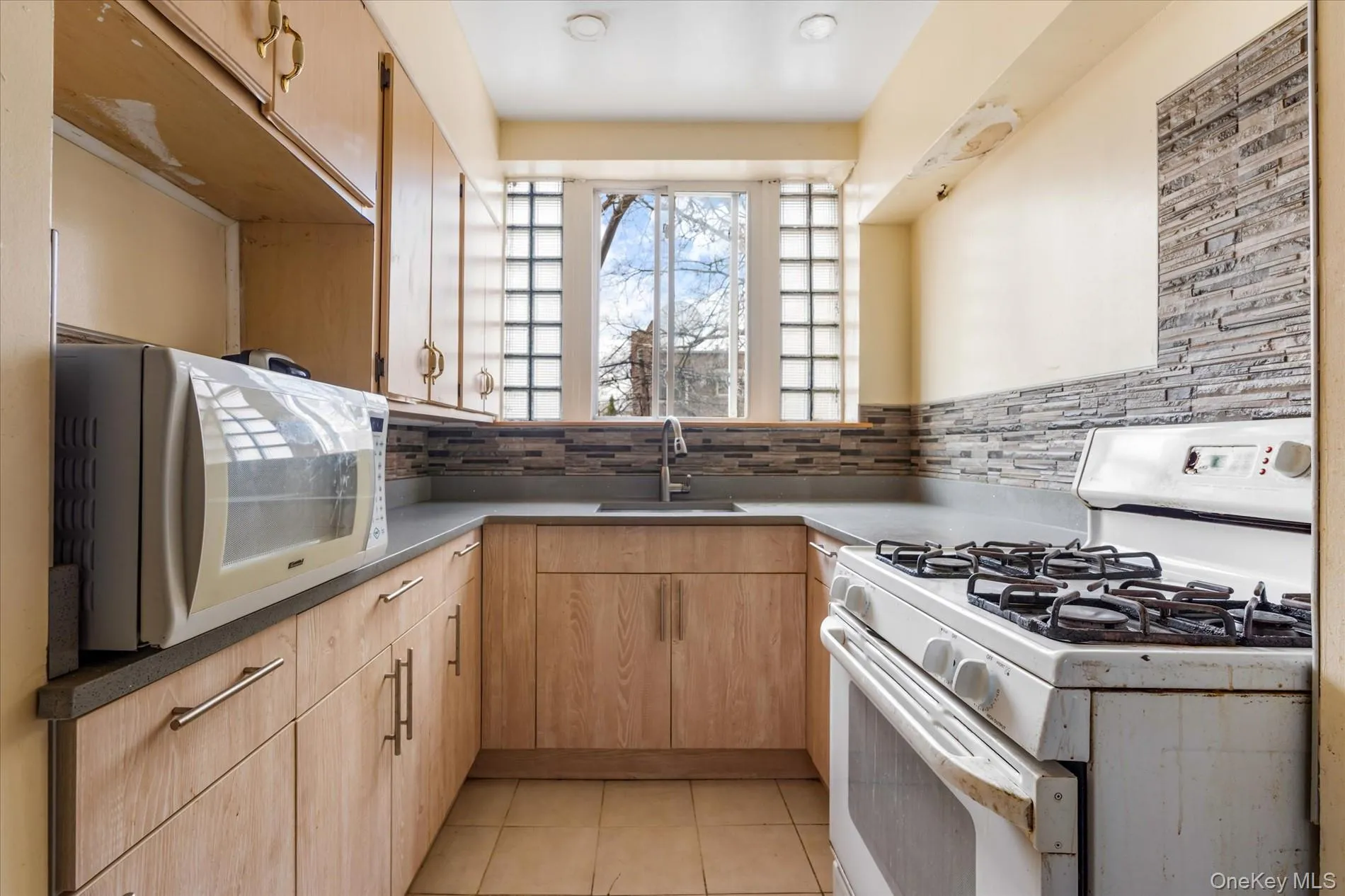 Kitchen featuring white appliances, a sink, light brown cabinets, light tile patterned floors, and tasteful backsplash Kitchen featuring white appliances, a sink, light brown cabinets, light tile patterned floors, and tasteful backsplash