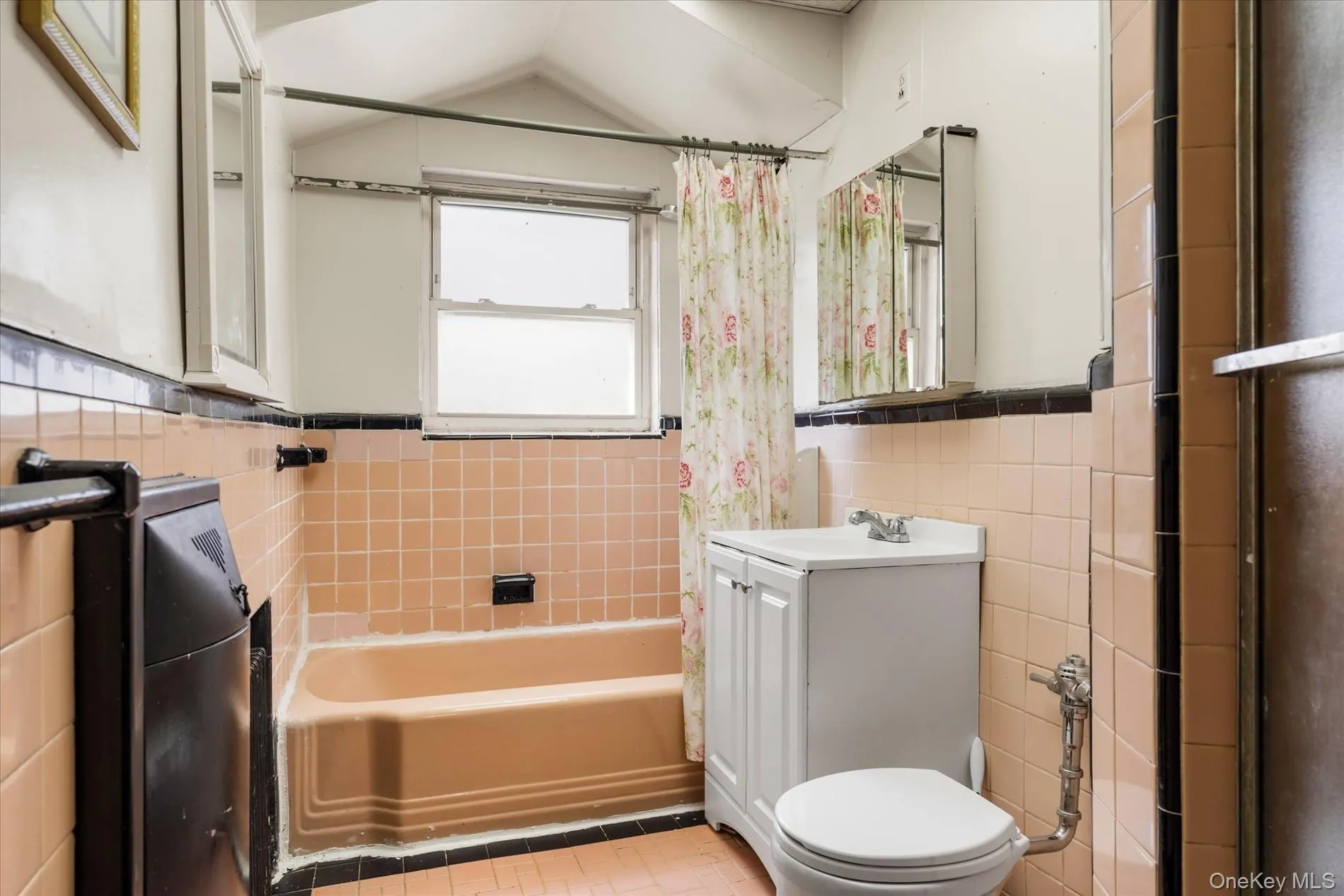 Bathroom featuring tile walls, toilet, a wainscoted wall, vanity, and shower / bath combo with shower curtain Bathroom featuring tile walls, toilet, a wainscoted wall, vanity, and shower / bath combo with shower curtain