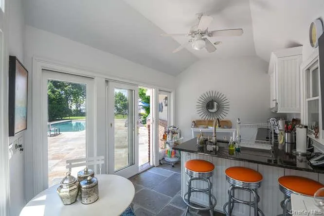 Kitchen featuring dark stone finish floors, a ceiling fan, lofted ceiling, white cabinets, and a peninsula Kitchen featuring dark stone finish floors, a ceiling fan, lofted ceiling, white cabinets, and a peninsula