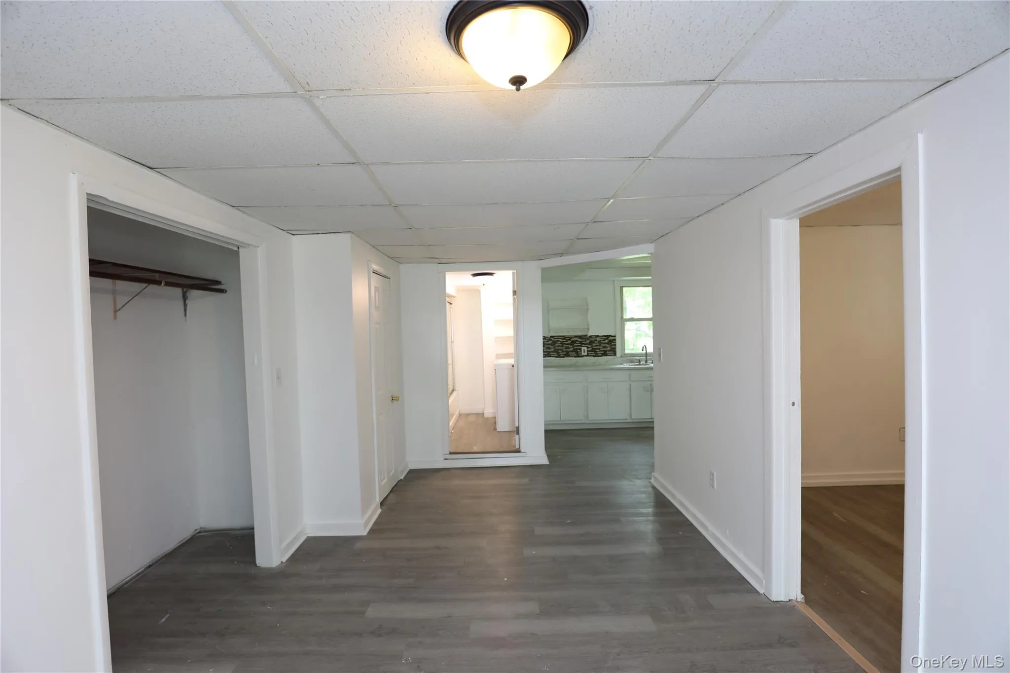Corridor featuring a drop ceiling, dark wood-type flooring, and baseboards Corridor featuring a drop ceiling, dark wood-type flooring, and baseboards