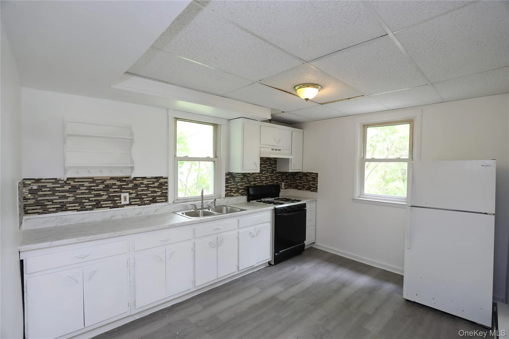 Kitchen featuring freestanding refrigerator, gas stove, a sink, healthy amount of natural light, and a paneled ceiling Kitchen featuring freestanding refrigerator, gas stove, a sink, healthy amount of natural light, and a paneled ceiling