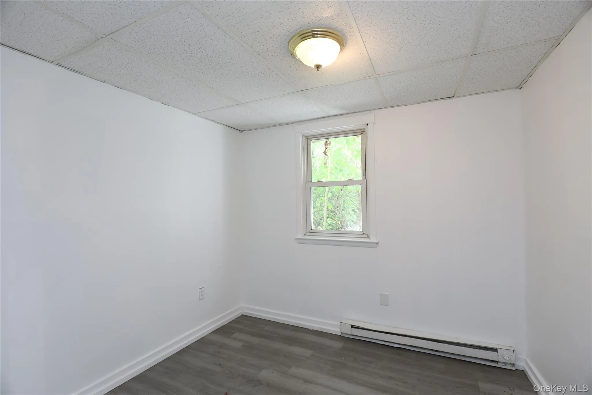 Empty room featuring baseboard heating, a paneled ceiling, dark wood finished floors, and baseboards Empty room featuring baseboard heating, a paneled ceiling, dark wood finished floors, and baseboards