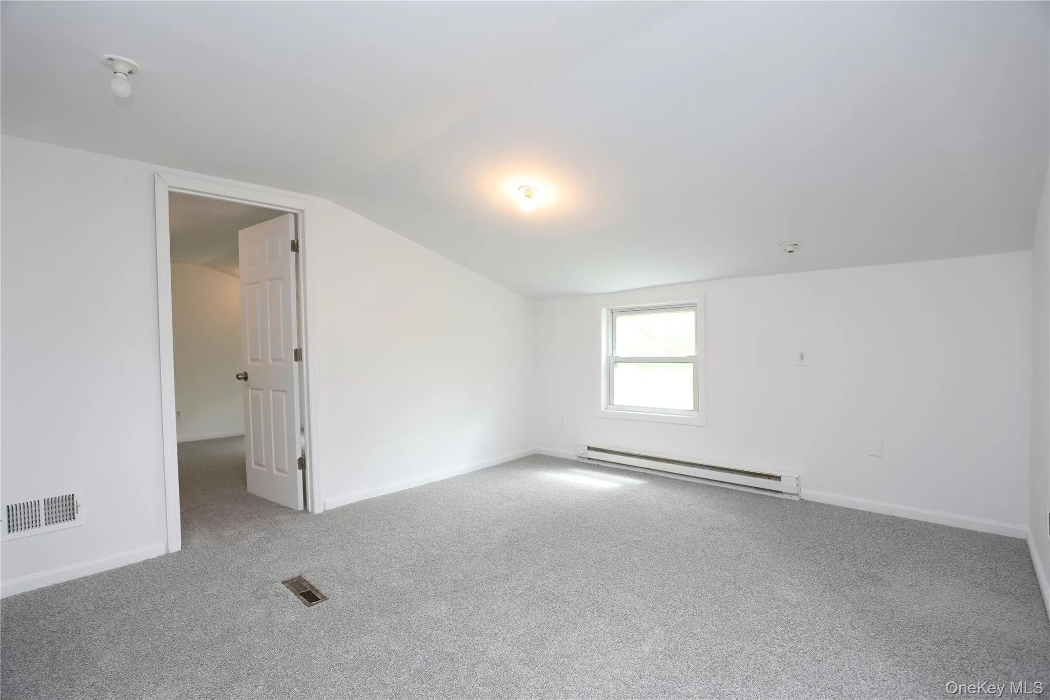 Empty room with baseboard heating, carpet floors, lofted ceiling, and baseboards Empty room with baseboard heating, carpet floors, lofted ceiling, and baseboards