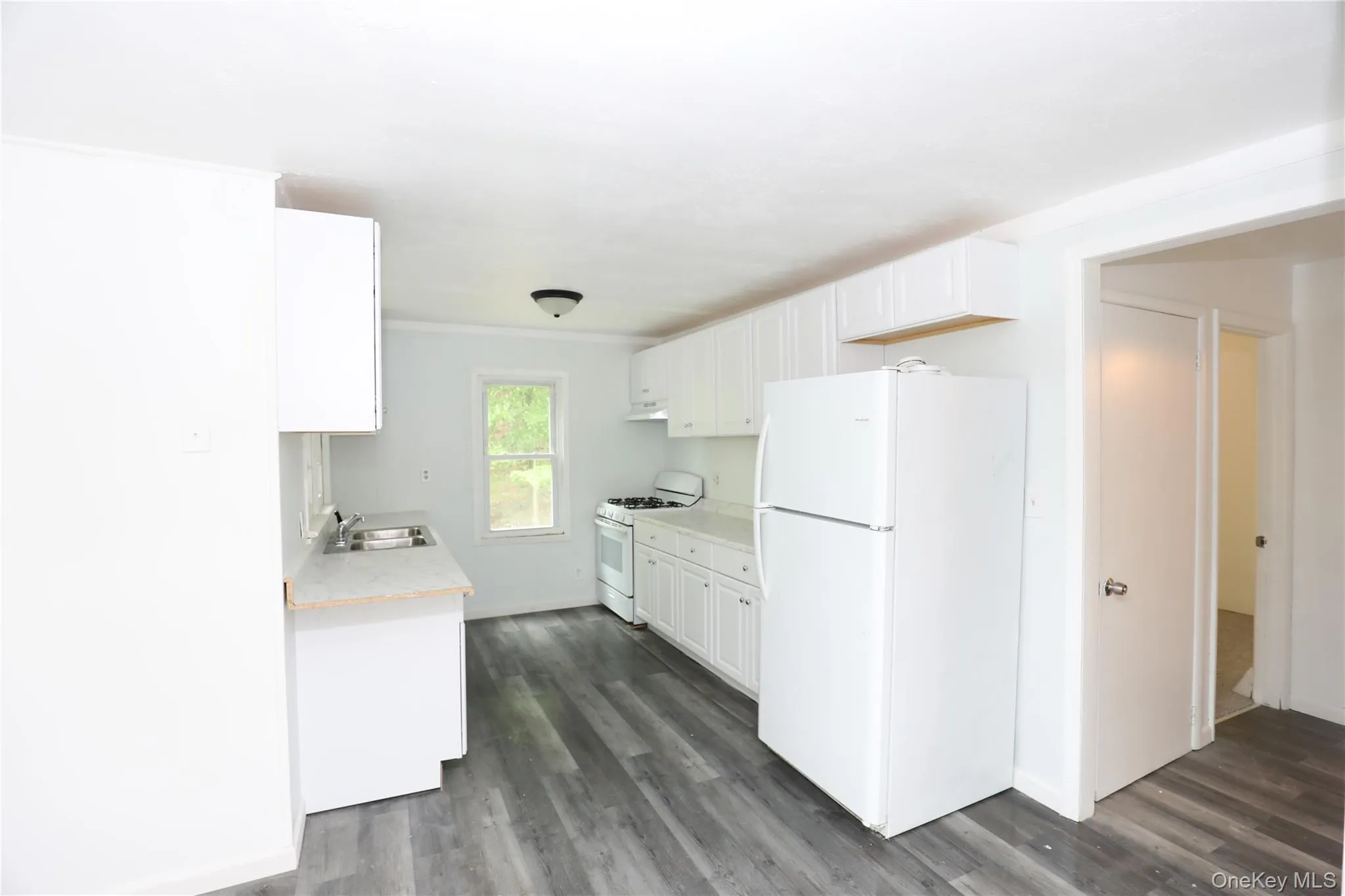 Kitchen with white appliances, a sink, light countertops, and dark wood-style flooring Kitchen with white appliances, a sink, light countertops, and dark wood-style flooring