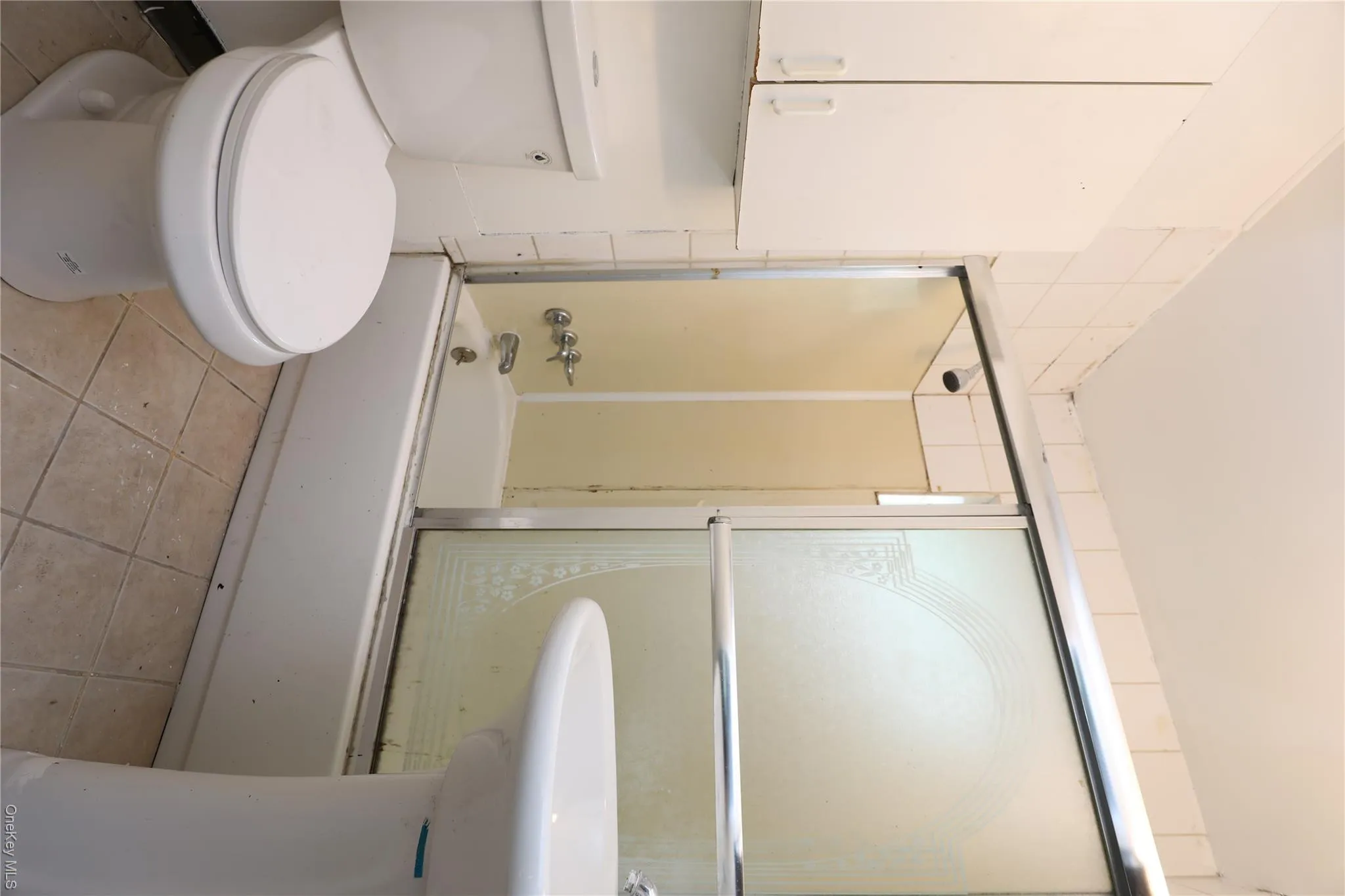 Full bathroom featuring tile patterned floors, shower / bath combination with glass door, and toilet Full bathroom featuring tile patterned floors, shower / bath combination with glass door, and toilet