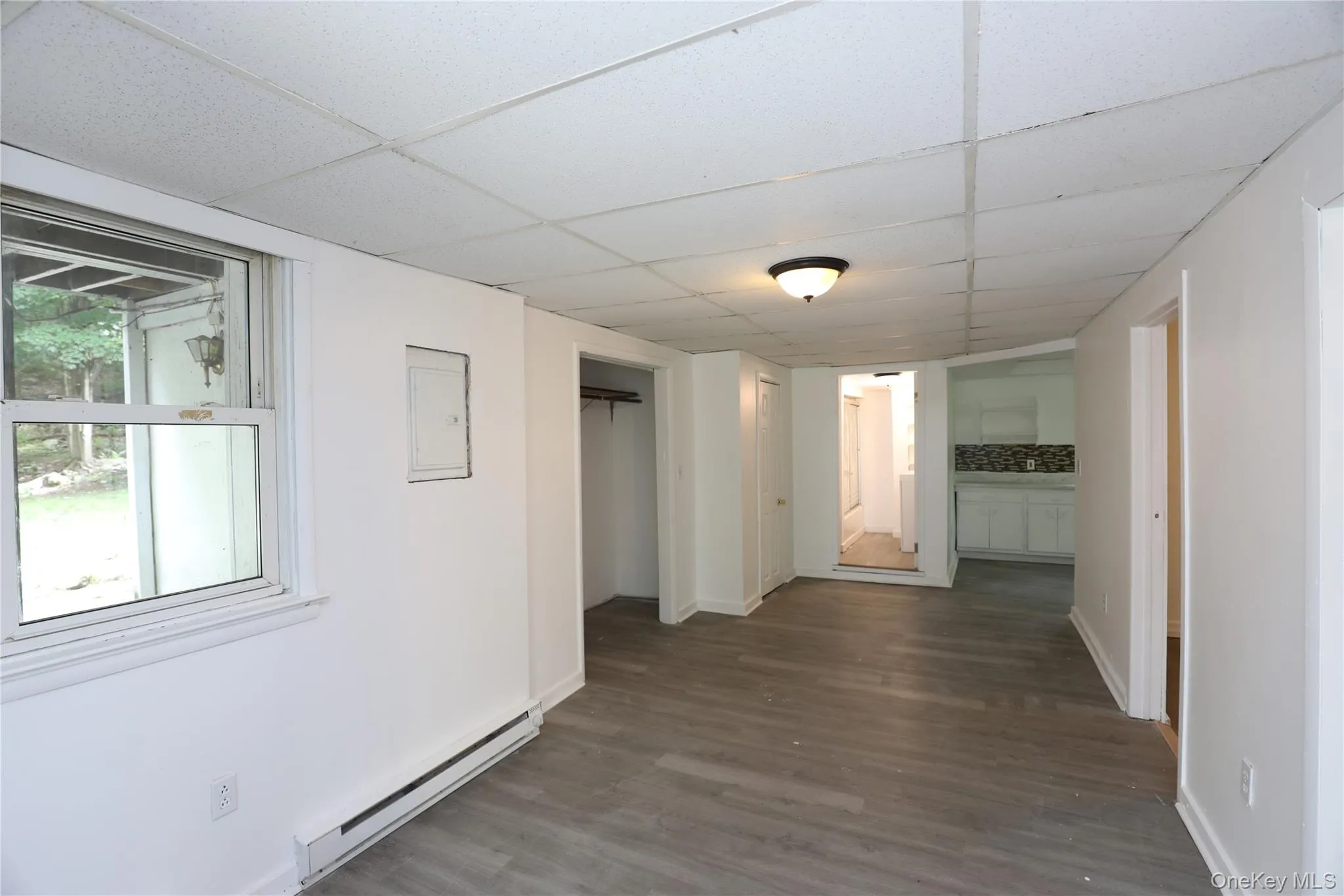 Corridor featuring baseboard heating, wood finished floors, a paneled ceiling, and baseboards Corridor featuring baseboard heating, wood finished floors, a paneled ceiling, and baseboards