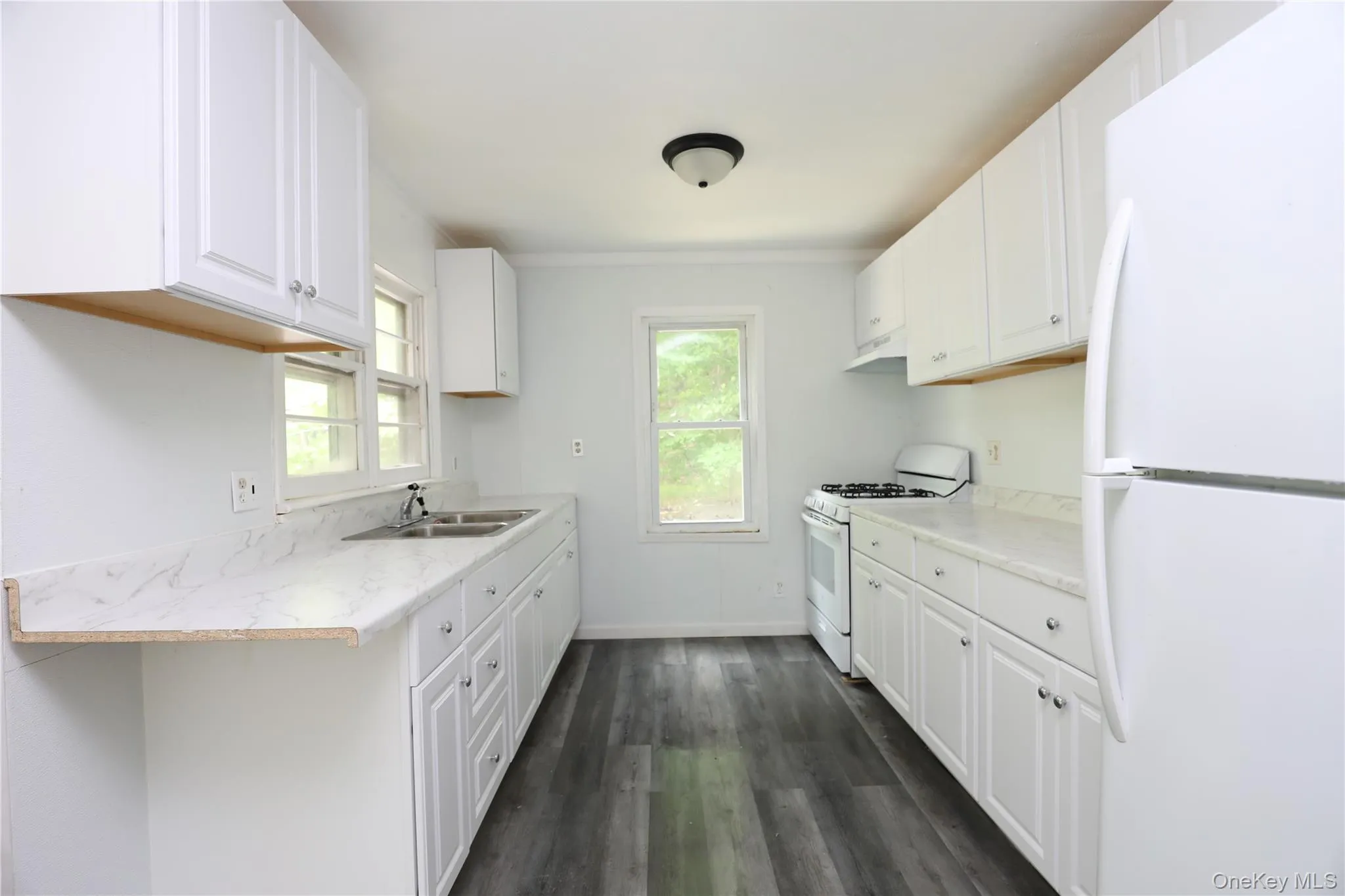 Kitchen featuring white appliances, a sink, dark wood-style flooring, white cabinetry, and baseboards Kitchen featuring white appliances, a sink, dark wood-style flooring, white cabinetry, and baseboards