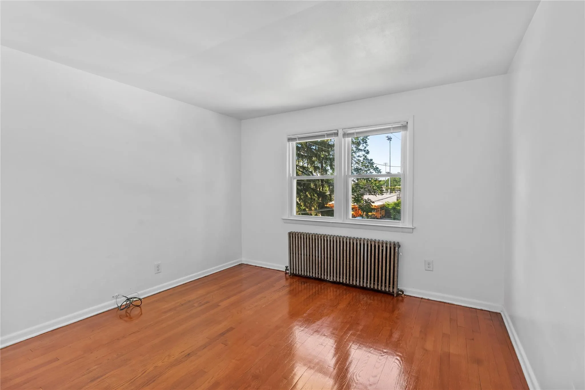 Spare room featuring radiator heating unit, wood finished floors, and baseboards Spare room featuring radiator heating unit, wood finished floors, and baseboards